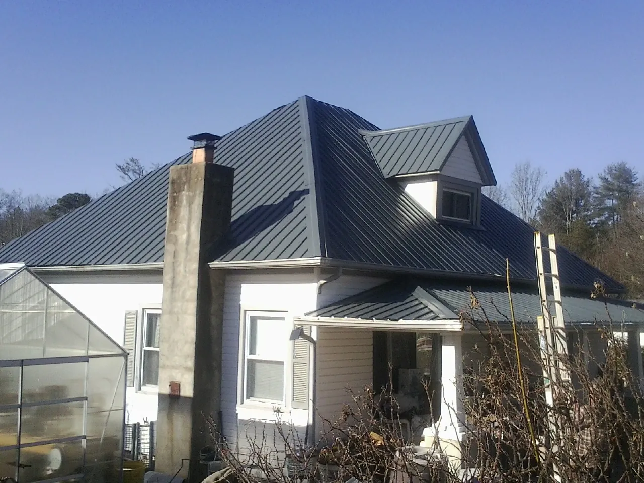 Dark blue standing seam metal roof on a white farmhouse with dormer — Slate & Tile Roof Repair by Roofing Brothers in Dousman