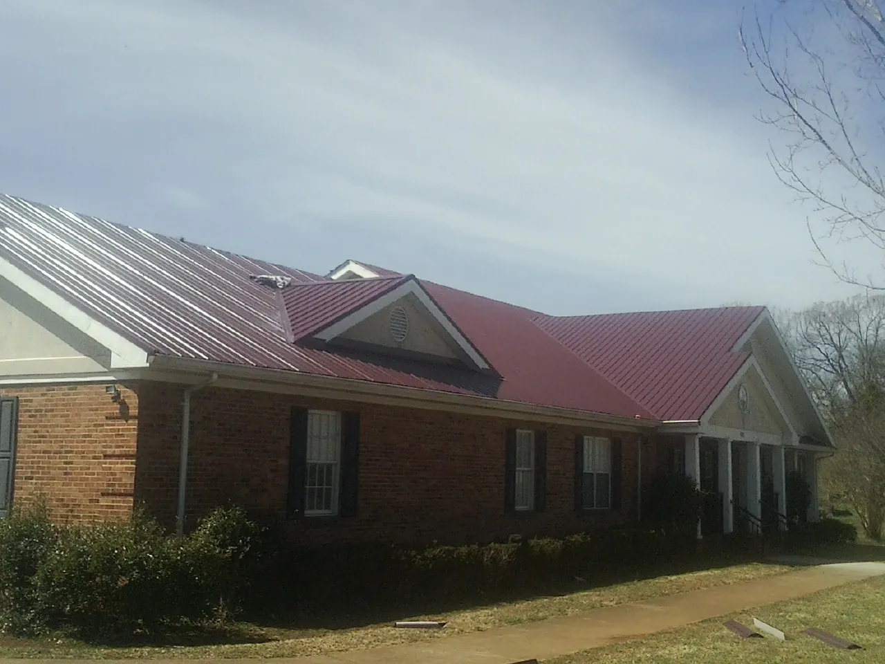 Red metal roof with gabled entries on a long brick building, from a Hail Damage Roof Repair job in Dousman