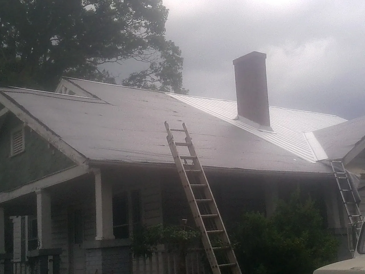 Ladders against a metal roof on an older home with a brick chimney in Dousman