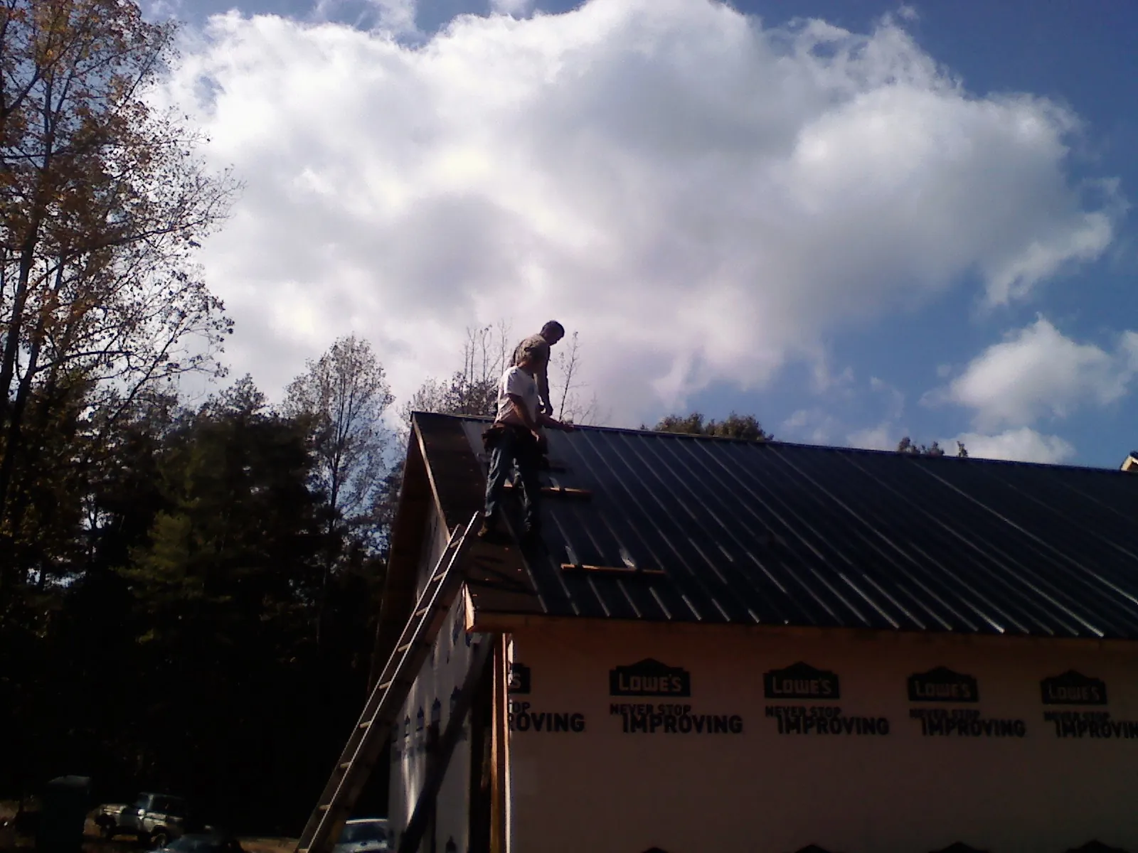 Roofer fastening dark metal panels high against a cloudy sky, from a Roof Inspection job in Dousman