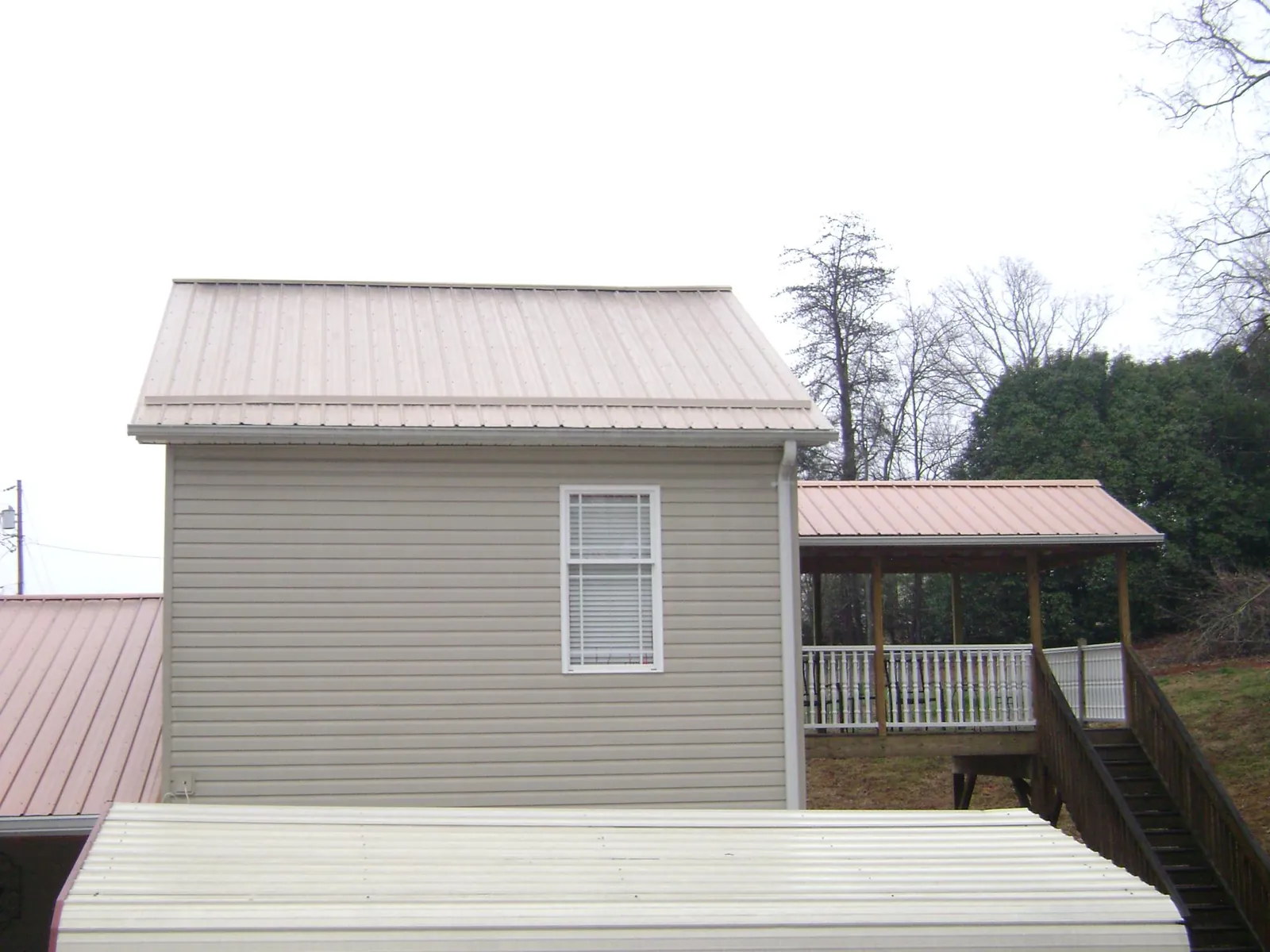 Tan metal roofs on a two story addition and attached porch, from a Roof Replacement job in Dousman